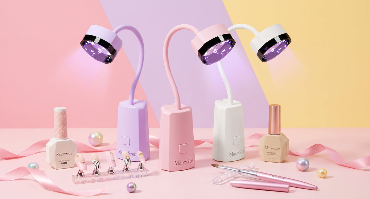 Three pastel UV LED nail lamp in lavender, pink, and white are arranged on a pink surface with pink ribbons, pearl-like beads, nail art tools, and small bottles. The lamps are lit with purple UV light.